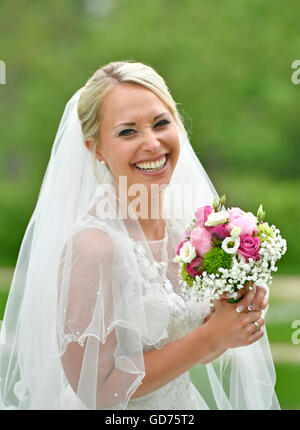 Lachende Braut im weißen Hochzeitskleid mit Brautstrauß und Schleier, Deutschland Stockfoto