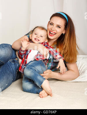 Mutter und Tochter zu Hause. Junge Mutter und Tochter umarmt. Mädchen in kariertes Hemd gekleidet. Tochter barfuß. Stockfoto