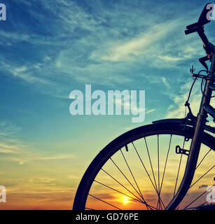 Schöne Nahaufnahme Szene des Fahrrades bei Sonnenuntergang, Sonne am blauen Himmel mit Vintage Farben Silhouette des Rad nach vorne zur Sonne Stockfoto