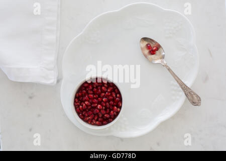 Top-Down Ansicht der Granatapfel Samen in einer Schüssel gesetzt auf einem Dessertteller auf weißem Marmor mit Serviette und Silberlöffel abgespeckt. Stockfoto