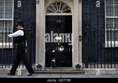 Larry, die die Katze vor der Tür sitzt, als ein Polizist vorbei an 10 Downing Street in London geht, wie David Cameron bereitet nehmen an die Versand-Box in das House Of Commons für seine letzte Sitzung Fragen als PM im House Of Commons vor der historischen Machtverschiebung stattfindet. Stockfoto