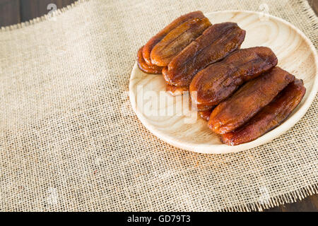 Getrocknete Bananendessert Thailand auf einer Platte aus Holz und Tuch Säcke auf dem Holzboden angeordnet. Stockfoto