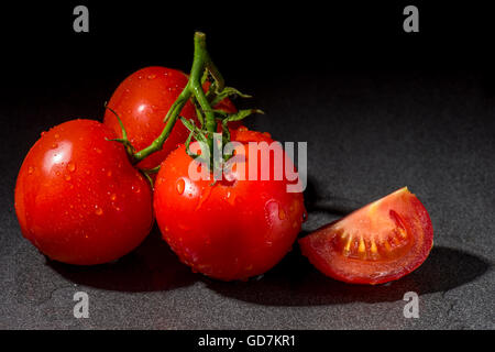 Drei frische Rebe reife Tomaten auf einem schwarzen Hintergrund. Stockfoto