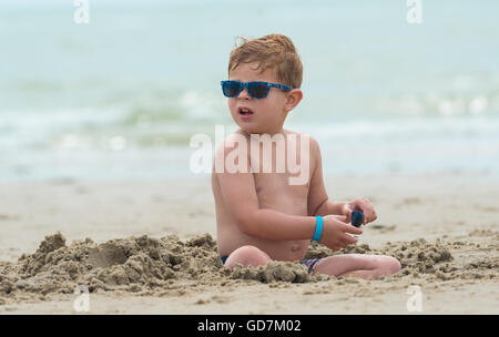 kleiner junge Kind am Strand mit Sonnenbrille sitzt das Kind in den Sand, schaut sich um
