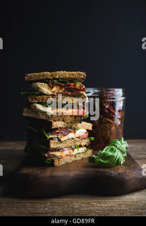 Caprese Sandwich oder Panini mit Vollkornbrot, Mozzarella, Cherry und getrockneten Tomaten, Basilikum auf Holzbrett über dunkle backgr Stockfoto