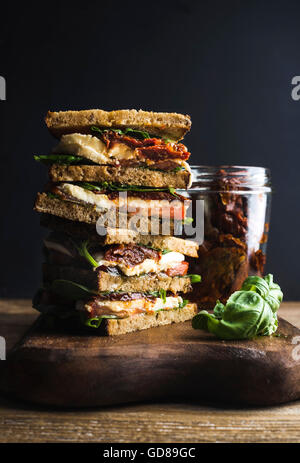 Caprese Sandwich oder Panini mit Vollkornbrot, Mozzarella, Cherry und getrockneten Tomaten, Basilikum auf Holzbrett über dunkle backgr Stockfoto