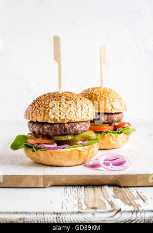 Zwei frische hausgemachte Burger serviert mit Zwiebelringen auf hölzernen Portion Brett auf weißem Hintergrund, Tiefenschärfe, vertikale comp Stockfoto
