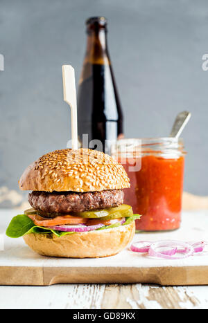 Frische hausgemachte Burger an Bord der weißen Holz serviert mit Zwiebelringen, Salsa-Sauce und Flasche Bier auf weißem Hintergrund, sele Stockfoto