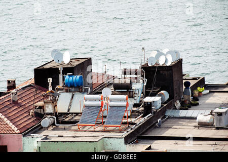 Ein Blick auf das Meer von der Dachterrasse mit Solarpaneelen, Satellitenschüsseln und Wassertanks zeigt städtische Technologielösungen für Energie und Kommunikation Stockfoto