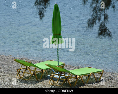 Zwei leere Lime Green Sonnenliegen mit einem geschlossenen Sonnenschirm Sonnenschutz auf einen Kiesstrand am Wasser Stockfoto