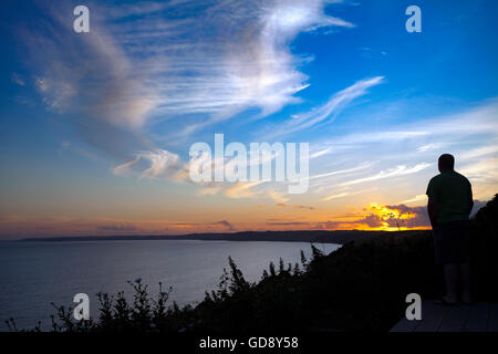 Eine Person beobachtet den Sonnenuntergang über Whitsand Bay an einem Sommerabend mit blauem Himmel und Wolken vom Weiler Freathy in Cornwall, England, UK Stockfoto