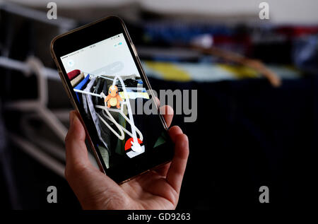 Berlin, Deutschland. 13. Juli 2016. Abbildung - ein "Pokémon Go" Spieler sein Smartphone, auf dem man das Pokémon "Glumanda" sitzen auf einem Wäscheständer in Berlin, Deutschland, 13. Juli 2016. Die app basiert auf realen Geodaten und führt seinen Nutzern von Ort zu Ort per GPS. Pokémon kann man auch in seiner eigenen Wohnung. Foto: Susann Prautsch/Dpa/Alamy Live News Stockfoto