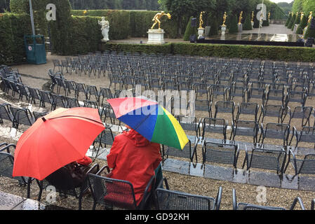 Hannover, Deutschland. 13. Juli 2016. Besucher mit Sonnenschirmen sitzen im Publikum in den Herrenhäuser Gärten für die Premiere von "Kleines Fest Im Grossen Garten" in Hannover, Deutschland, 13. Juli 2016. Eine Gewitter mit Blitz und Donner, Regen und Sturm verursacht die Beendigung des ersten abends des Kunstfestivals. Foto: Julian Stratenschulte/Dpa/Alamy Live News Stockfoto