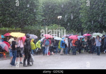 Hannover, Deutschland. 13. Juli 2016. Besucher mit Regenschirmen stehen in den Herrenhäuser Gärten bei der Premiere von "Kleines Fest Im Grossen Garten" in Hannover, Deutschland, 13. Juli 2016. Eine Gewitter mit Blitz und Donner, Regen und Sturm verursacht die Beendigung des ersten abends des Kunstfestivals. Foto: Julian Stratenschulte/Dpa/Alamy Live News Stockfoto