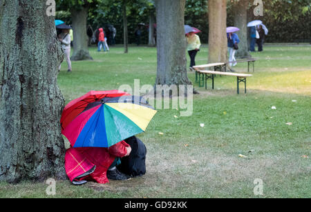 Hannover, Deutschland. 13. Juli 2016. Besucher mit Regenschirmen Barsch unter einem Baum in den Herrenhäuser Gärten bei der Premiere von "Kleines Fest Im Grossen Garten" in Hannover, Deutschland, 13. Juli 2016. Eine Gewitter mit Blitz und Donner, Regen und Sturm verursacht die Beendigung des ersten abends des Kunstfestivals. Foto: Julian Stratenschulte/Dpa/Alamy Live News Stockfoto