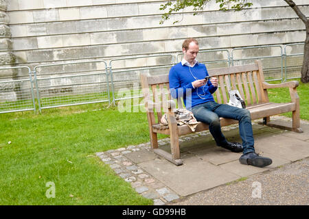 Ein Mann sitzt auf einer Bank auf seinem iPod in St James Park in London auf seinem Handy hören Stockfoto