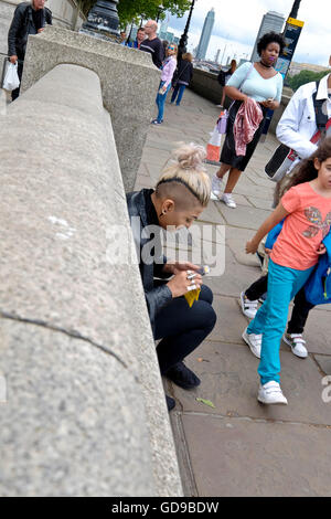 Eine Frau mit einer alternative Frisur rollt eine Zigarette auf der Victoria Embankment am Londoner Themse Stockfoto