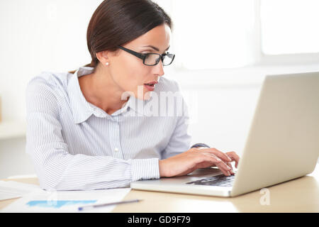 Lateinischen hübsche Rezeptionistin mit Brille arbeiten auf dem Laptop während der Suche schockiert Stockfoto