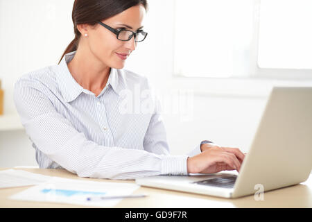 Lächelnde Frau Mitarbeiter mit Brille arbeiten am Laptop auf ihrem Schreibtisch Stockfoto