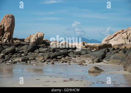 Felsen an einem Strand mit Bergen im Hintergrund Stockfoto