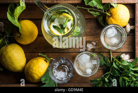 HAUSGEMACHTE Limonade mit Minze, Eis und frischen Zitronen serviert mit frischen Zitronen und Minze auf Holztablett Hintergrund, Ansicht von oben Stockfoto