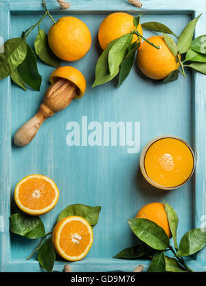 Glas frisch gepressten Orangensaft und Orangen mit Blättern auf hölzernen Türkis Blau bemalten Hintergrund. Ansicht von oben, Textfreiraum Stockfoto