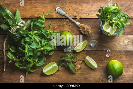 Zutaten für die Herstellung von Mojito Sommer cocktail. Haufen frischer Minze, Limetten, brauner Zucker und Eis über rustikalen hölzernen Hintergrund, Top v Stockfoto