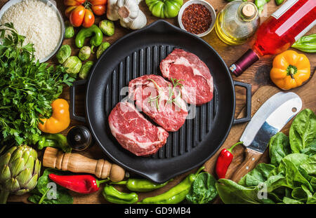 Zutaten für gesundes Fleisch Abendessen kochen. Roh, ungekocht Rindersteaks in Gusseisen Grillen Pfanne mit Gemüse, Reis, Gewürze, o Stockfoto