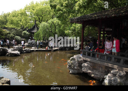 Ein Haus, ein Teich, Goldfisch, Vegetation, eine Brücke und Touristen im 16. Jahrhundert Yuyuan Garten, ein typischer klassischer Garten. Stockfoto