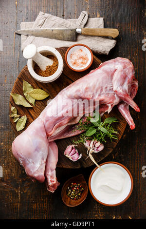 Rohe ganzes Kaninchen und Zutaten für das Kochen auf dunklem Holz Stockfoto