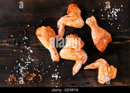 Roh mariniertes Fleisch Hähnchenflügel und Beine für BBQ mit Gewürz-Salz und Pfeffer in dunklem Holz. Ansicht von oben Stockfoto
