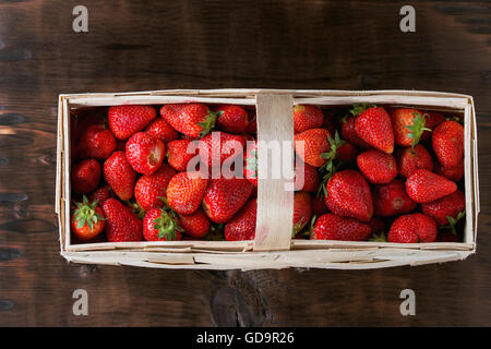 Frische reife Saft Erdbeeren in Holz quadratische Korb in dunklem Holz. Ansicht von oben Stockfoto