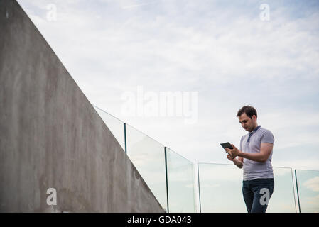 Porträt von stilvollen hübscher junger Mann im Freien stehen. Mann trägt T-shirt mit Tablet-PC Stockfoto
