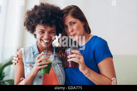 Porträt von glücklichen jungen Freunde trinken Saft aus frischen Früchten zusammen. Zwei Frauen stehen zusammen trinken Saft und mit Blick auf c Stockfoto