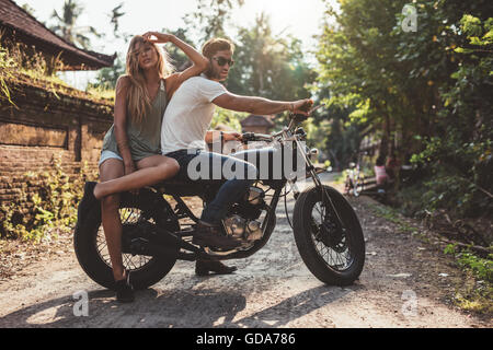 Porträt des jungen Paares in der Landschaft mit Motorrad hängen. Junger Mann und Frau auf dem Motorrad. Stockfoto