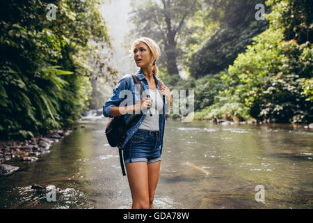 Porträt von schöne junge Frau mit Rucksack durch den Bach. Weibliche Wanderer Wandern durch den Gebirgsbach. Stockfoto