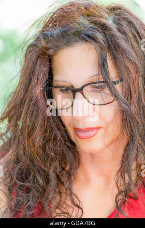 wunderschöne Frau mittleren Alters in einem roten Kleid und langen braunen welliges Haar ist das Tragen einer Brille nerdy lesen Stockfoto