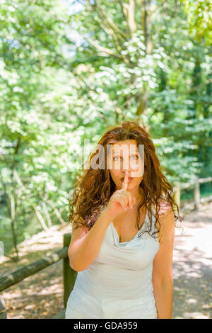 Kurvige edel Reife Frau legen Zeigefinger an Lippen Schweigen in einem Garten Stockfoto