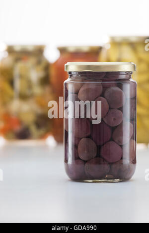 Eingelegte schwarze Oliven Glas mit anderen Gurken Gläser im Hintergrund Stockfoto