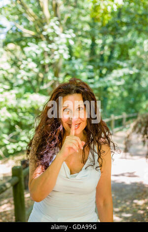 Kurvige edel Reife Frau legen Zeigefinger an Lippen Schweigen in einem Garten Stockfoto