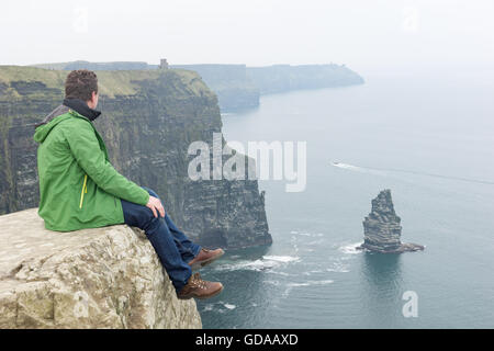 Irland, County Clare, Cliffs of Moher, Man sitzt hoch auf einem Felsen Stockfoto