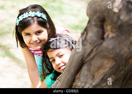 2 indische Kinder Mädchen nur Freunden Parken Baumstamm stehend Versteckspiel Stockfoto