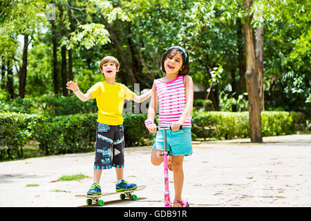 2 Indianer Kinder Jungen und Mädchen Freunden Push Scooter fahren und Skateboard Skaten Stockfoto