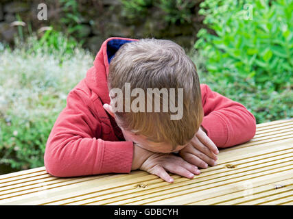 Junge, zwei Jahre alt, an einem Tisch sitzen und traurig Stockfoto