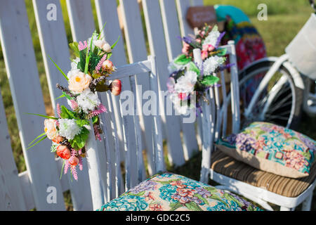 Schöne offene Terrasse im Garten mit Tiffany farbige alten weißen Stühlen, bunte samt Kissen und Zaun, Palisade, Fahrrad auf Hintergrund dekoriert Blüten im Boho-Stil. Stockfoto