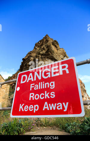 Ein "Steinschlag Gefahr fernzuhalten" Schild mit Klippen hinter. In Staithes, North Yorkshire, England. Stockfoto