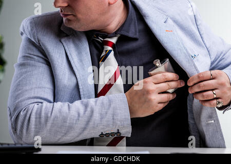 Büroangestellte, die einen Kolben in seine Innentasche, Dring am Arbeitsplatz versteckt, weil er flüssigen Tapferkeit braucht Stockfoto