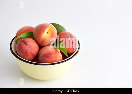 Reife Pfirsiche mit Blättern in einer Zitronengelb Schüssel auf einem weißen Hintergrund. Stockfoto