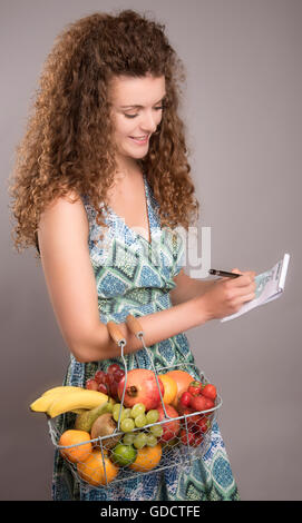 Junge Frau mit einem Warenkorb von frischen Früchten Überprüfung eine Einkaufsliste Stockfoto