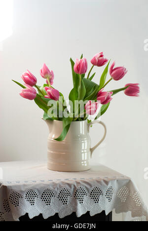 Rosa Tulpen in weißer Krug auf Spitzen Tischdecke Stockfoto